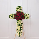 White rose standing cross — white roses along the arms and base with a red rose cluster at the center crossing, backed by Italian ruscus foliage on a wooden easel | Ecoroses Los Angeles