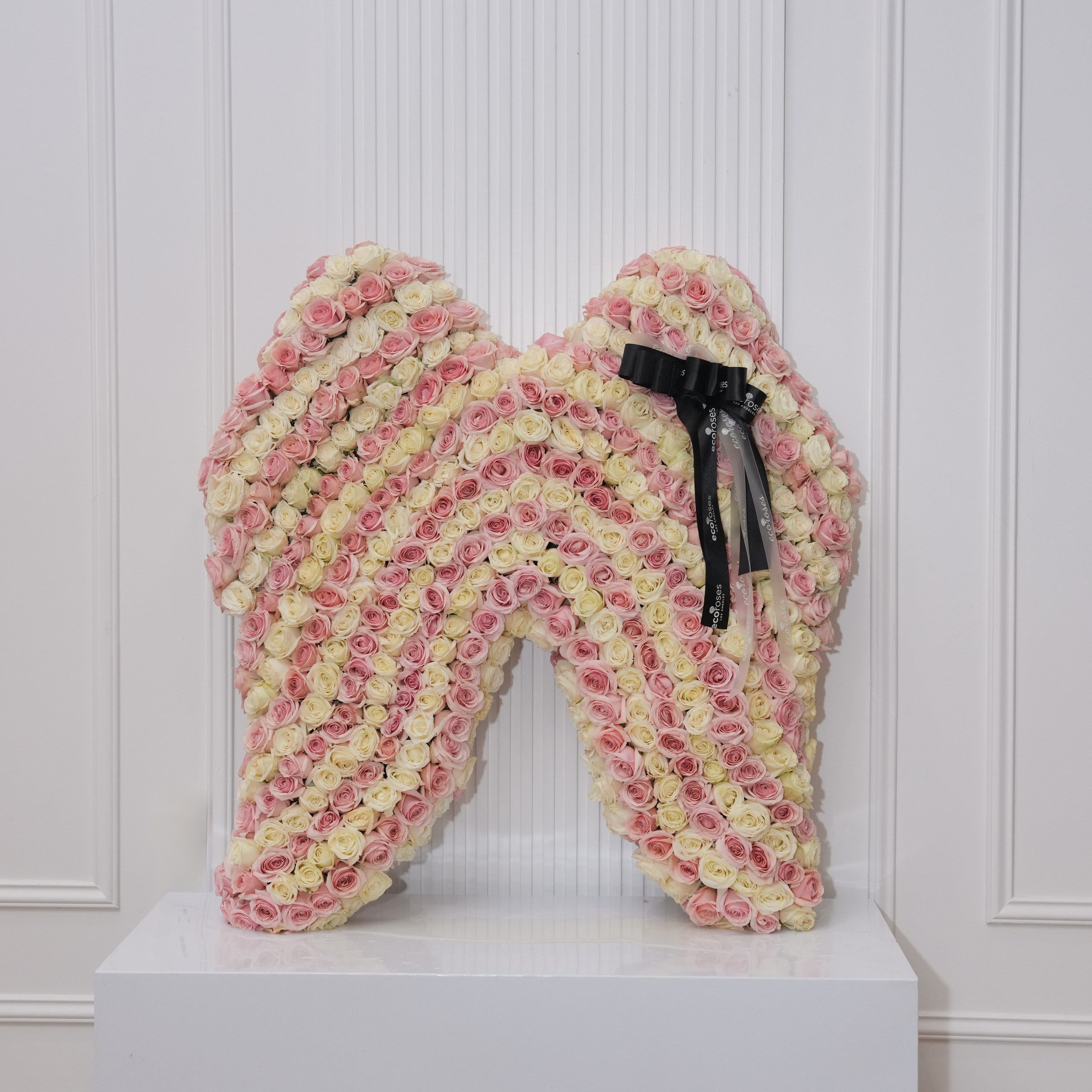Angel wings memorial — pink and cream baby roses densely sculpted into an angel-wing silhouette on a white pedestal | Ecoroses Los Angeles